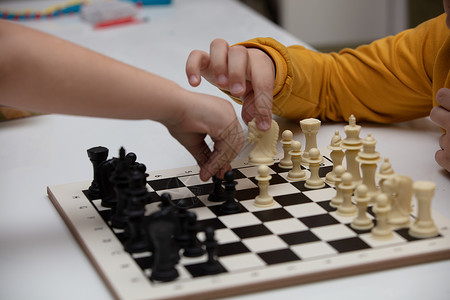 坐在一张桌子下棋 孩子全神贯注于游戏 思考着下一步该往哪里走 早期发展 儿童家庭教育游戏战略学习玩家爱好木板闲暇童年比赛运动数字背景