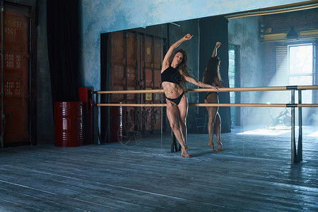 一个漂亮的运动员身材的女孩 一个芭蕾舞演员站在一个大型阁楼式健身房的交际舞机前 一面巨大的镜面墙 窗外的日光身体运动冒充体操酒吧背景图片