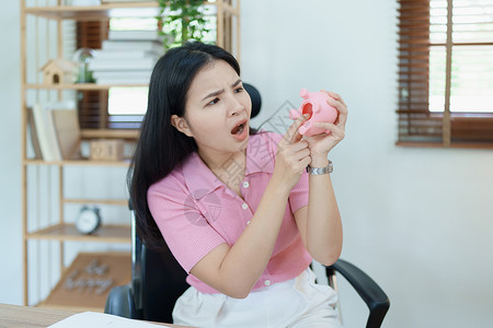卖粽子的猪一位亚洲女商务人士在中小企业业务中表现出严肃而焦虑的表情 但粉红猪存钱罐里没有钱 储蓄计划购物技术营销计算经理银行业桌子成人平衡背景