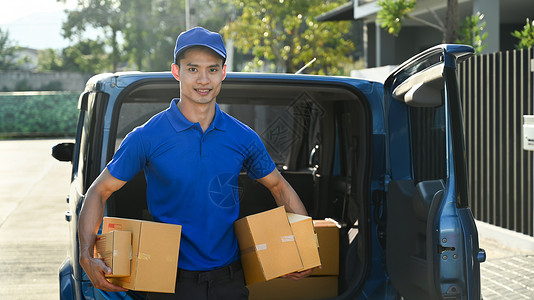 身穿蓝制服 手拿着纸板的送货员在露天送货面包车前行在职的高清图片素材