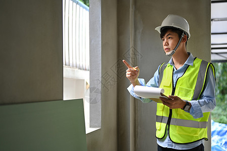 穿着安全头盔和防伪衣的青年男子检查员 手持剪贴板 检查重建后的建筑工作职场职业领班建筑师财产项目工地男人建筑工人背景图片