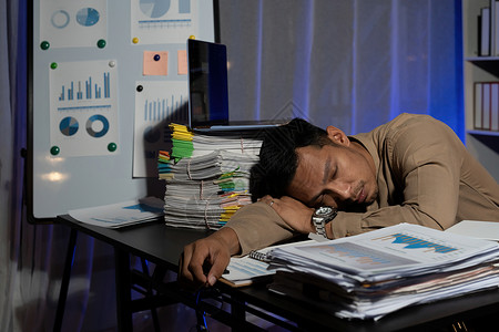 精疲力尽的商务人士睡在办公桌前 深夜加班 他被成堆的文书工作包围管理人员商业睡眠员工笔记本商务项目办公室经理桌子最后期限高清图片素材