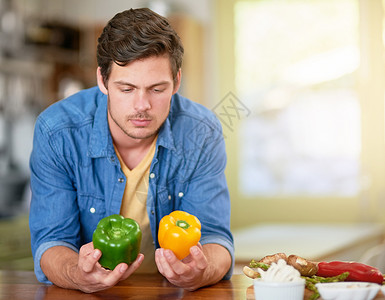 我应该选择黄色还是青椒 一个年轻人站在家里的厨房里决定用哪种或胡椒做饭图片