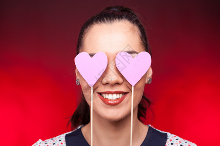 微笑的快乐的女人 用两颗粉红的心遮着她的眼睛肖像高清图片素材