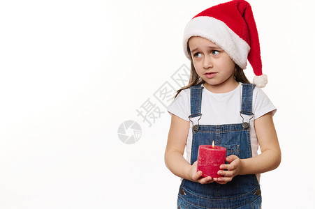 点蜡烛的孩子戴着圣诞老人帽子的美感小姑娘 拿着点蜡烛 许愿 寻找白色背景文字的复制空间背景