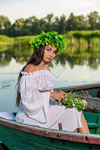 深色头发长发的女神 穿着白色古董礼服 坐在河中央的一条船上魔法花朵裙子神话海滩若虫童话魅力成人冒充美人鱼高清图片素材