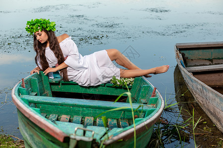 深色头发长发的女神 穿着白色古董礼服 坐在河中央的一条船上神话裙子冒充童话美人鱼魔法魅力若虫花朵女孩漂亮的高清图片素材
