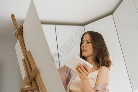 年轻女艺术家在卧室的画架上在画布上绘画  艺术和创意概念职业阳光快乐工作女士女性艺术品画家帆布画廊人高清图片素材