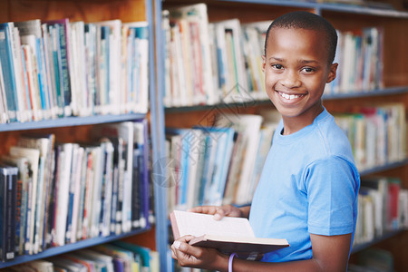 故事就像新的游乐场 一个非裔美国男孩的肖像在图书馆享受一本好书 (笑声)背景图片