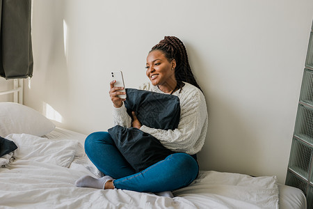 快乐的现代非洲裔美国年轻女孩谈论视频聊天并坐在家里交流的概念 微笑的时髦女孩在家里用电话制作自画像消息工具拍照相机手机成人卷发女自然的高清图片素材