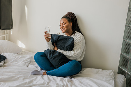 快乐的现代非洲裔美国年轻女孩谈论视频聊天并坐在家里交流的概念 微笑的时髦女孩在家里用电话制作自画像相机手机会议技术跨国辫子房间卷女士高清图片素材