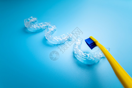 蓝色背景的透明对齐者 有明黄色牙刷 牙科主题背景图片