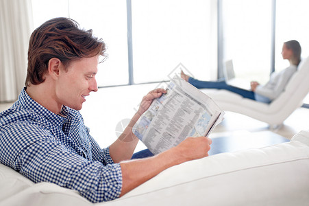 计划在家里过一个懒惰的一天 一个年轻男人和他搭档一起看报纸 背着背景生活方式高清图片素材