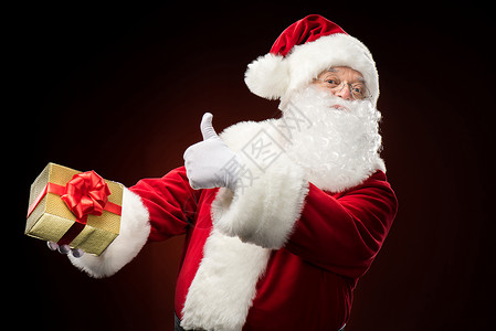手拿着礼物盒的圣诞老人 打手势 圣诞节的时候 竖起大拇指 传统的背景图片