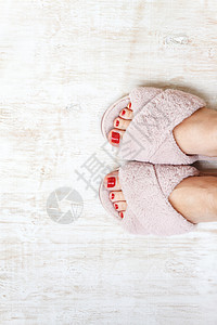 毛毛拖鞋双脚和红指甲 在家庭毛毛 毛毛的粉红色拖鞋上 凉鞋 地面背景