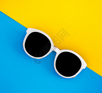 时尚的白色太阳镜在明亮蓝色和黄黄色背景上 顶部视图 孤立 复制空间 塑料 海滩背景图片