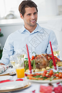 圣诞晚宴设置圣诞晚宴桌边坐着的迷人男人 用餐 蔬菜 快乐的 烤肉晚餐背景