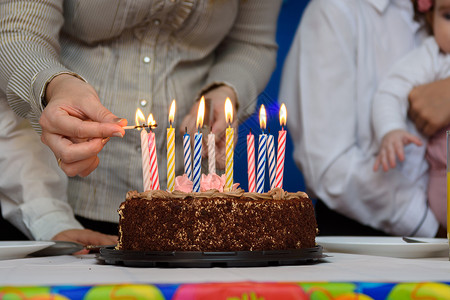 妈妈在生日派对上 在蛋糕上点蜡烛 手背景图片