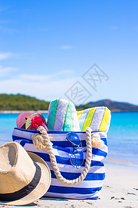 白沙滩上的蓝包 草帽 翻滚式拖鞋和毛巾 眼镜背景图片