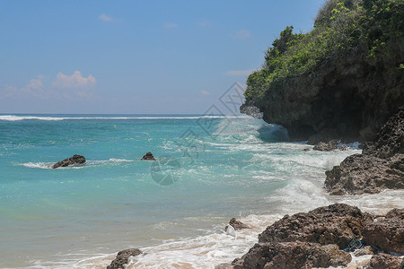 海滩与巴厘岛的金色细沙 当海浪拍打海岸的岩石悬崖时 绿松石蓝色的海水变成了海中的泡沫 与蓝天的晴天 旅游自然概念 海洋 火山背景图片