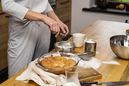 做糕点橡木桌上的美味苹果派 配料 穿着灰色睡衣的女人在阁楼风格的厨房里做美味的苹果派 牛奶 鸡蛋 糖和桌上的烤馅饼 家庭厨房 面包师背景