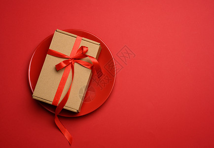 长方形棕色纸板盒 用丝绸红丝带绑在圆陶瓷红色板上 派对 约会背景图片