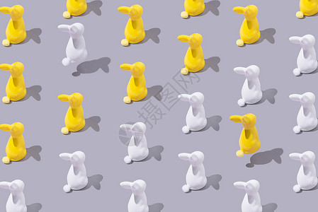 灰色背景上带有黄色和白色塑料兔子的创意图案 极简主义理念背景图片
