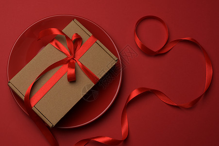 长方形棕色纸板盒 用丝绸红丝带绑在圆陶瓷红色板上 磁带 天背景图片
