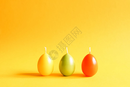 黄色彩蛋传统的复活节装饰 黄色背景上彩蛋形的一组明亮燃烧的石蜡蜡烛 手工制作的背景