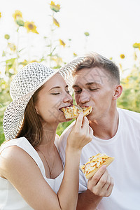 小情侣在日落的向日葵田野野餐 一起咬一块披萨衬衫高清图片素材
