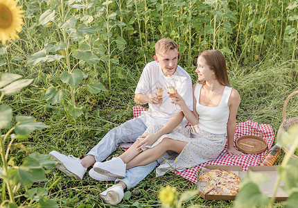 日落时在向日葵田野野餐的年轻夫妇 喝 食物草高清图片素材