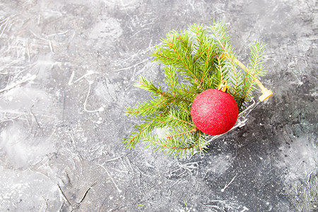 在黑色背景 复制空间的小型购物小车厢里 制作绿色绿枝和红色闪亮圣诞树玩具球 礼物背景图片