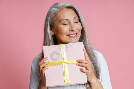 丰满成熟的亚洲女士拿着带丝带的礼物盒 披着粉红色背景图片