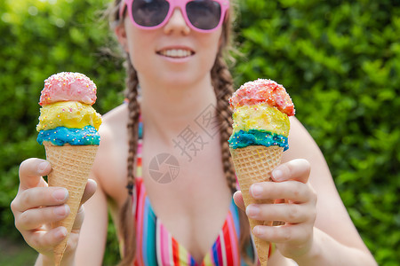 盛夏穿彩虹色泳衣 粉红太阳眼镜和芭蕾舞快乐假期 周日概念的花边喷洒着羊水的美丽女孩 手握两个多彩的冰淇淋 小雨 自然背景图片