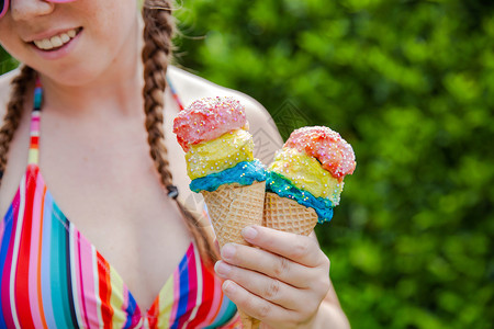 盛夏穿彩虹色泳衣 粉红太阳眼镜和芭蕾舞快乐假期 周日概念的花边喷洒着羊水的美丽女孩 手握两个多彩的冰淇淋 复古的 巧克力背景图片