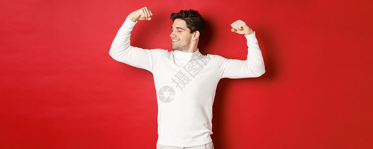 穿着白色毛衣 微笑着的帅哥的画像 弯曲二头肌 用力量吹牛 锻炼后炫耀强壮的肌肉 站在红色背景上 派对 脸背景图片