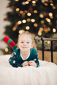 小caucasians 女孩躺在床上 在圣诞树旁边的床和微笑花环高清图片素材