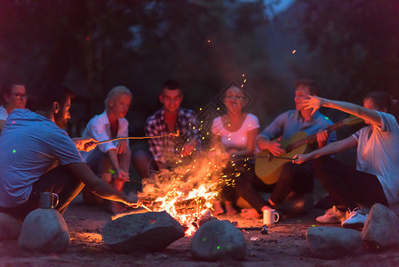 篝火音乐年轻朋友在营火周围放松 享受 火焰 野餐 坐着背景