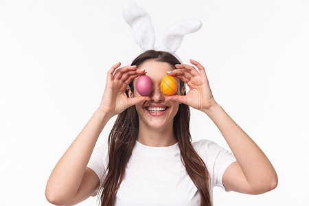 复活节 假期和春天的概念 欢快 热情的年轻女子庆祝复活节的特写肖像 她的眼睛上拿着彩色鸡蛋 微笑着 白色背景 快乐的 兔子女孩高清图片素材