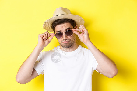 旅游和度假概念 关闭乘坐旅行假期 佩戴带草帽的墨镜 黄色背景的凉凉酷游客 以享受节假日; 成功 咧着嘴笑背景图片