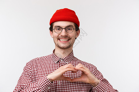 特写肖像可爱的留着胡须的白人男性戴着眼镜和红色的帽子 微笑着高兴 表现出心的姿态 表达爱或同情 爱的人 站在白色背景乐观衬衫高清图片素材