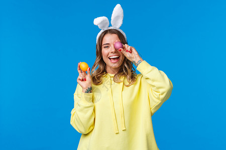 假期 传统和庆祝概念 欢快快乐的年轻漂亮女性庆祝复活节 展示两个彩蛋 笑着 戴着可爱的兔耳 蓝色背景 漂亮的 教育兔子高清图片素材