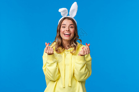 假期 传统和庆祝概念 欢快的欧洲女孩庆祝复活节 戴着兔耳展示韩国红心标志 欢快地微笑 站在蓝色背景手高清图片素材