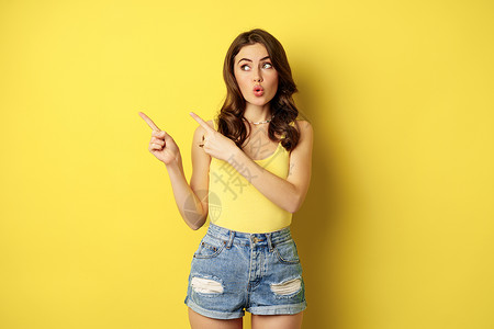 时尚的夏日女孩的肖像 褐发女人露出路来 指左手 广告 站在黄色背景上 脸 快乐喜悦高清图片素材