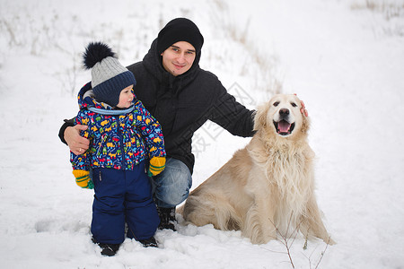 爸爸和儿子在雪地里跟狗玩 金色寻宝游戏图片