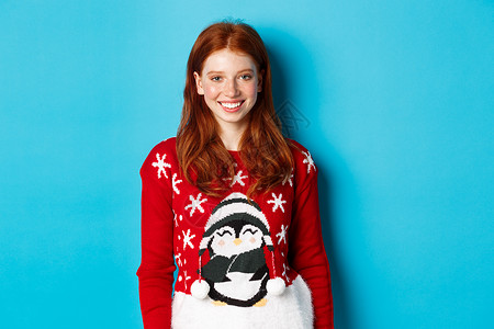 寒假和平安夜的概念 可爱的微笑少女 红头发 穿着滑稽的圣诞毛衣 站在蓝色背景下 女孩 美丽的背景图片
