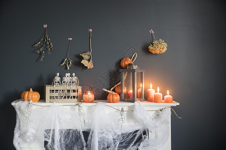 万圣节家居装饰 深蓝色墙壁壁炉旁木箱中的塑料玩具骨架 骷髅花环 梳妆台上的蜘蛛网 橙色蜡烛和灯笼 绳索 盒子背景图片