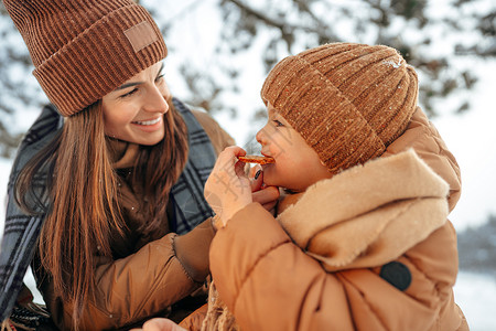年轻女子和儿子在冬季森林野餐喝热茶 幸福 热水瓶图片