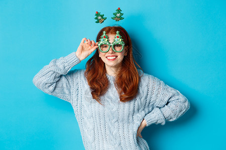 寒假和圣诞节销售理念 庆祝新年的漂亮红发女模特 戴着滑稽的派对头带和眼镜 对着镜头微笑 购物 学生背景图片