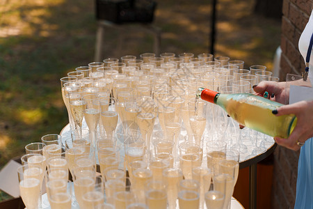 服务员将香槟倒在可支配塑料葡萄酒杯中 在森林欢迎饮料区 将闪亮的红酒投入酒杯 庆祝 酒吧吐司高清图片素材